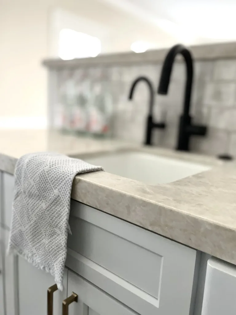 Matte black faucet over a farmhouse sink with hand-glazed backsplash tile and brass drawer pulls