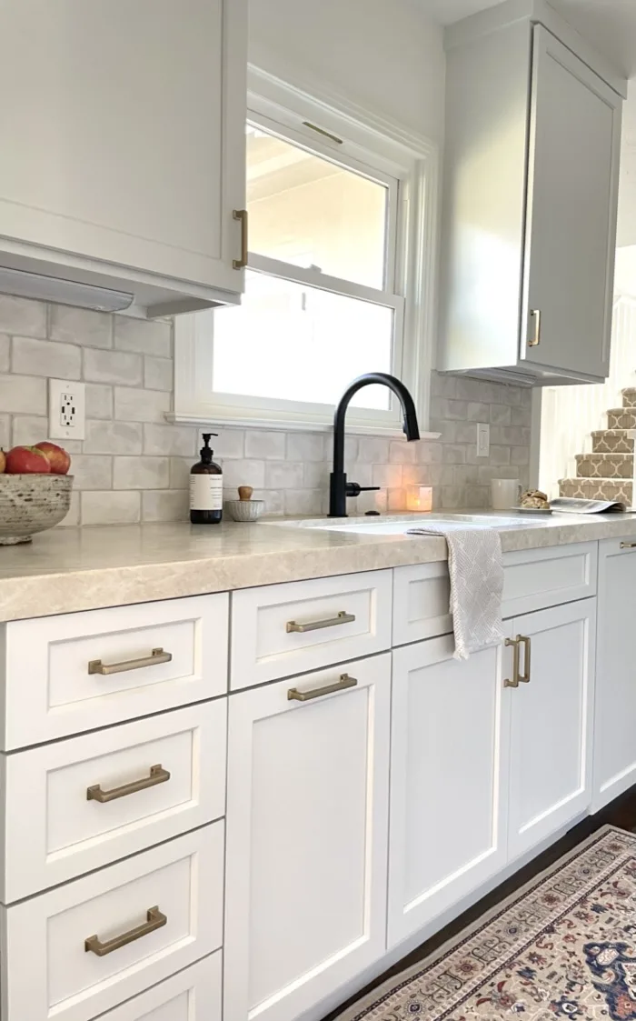 Galley kitchen view toward the farmhouse sink with matte black faucet, brass hardware, and Persian runner