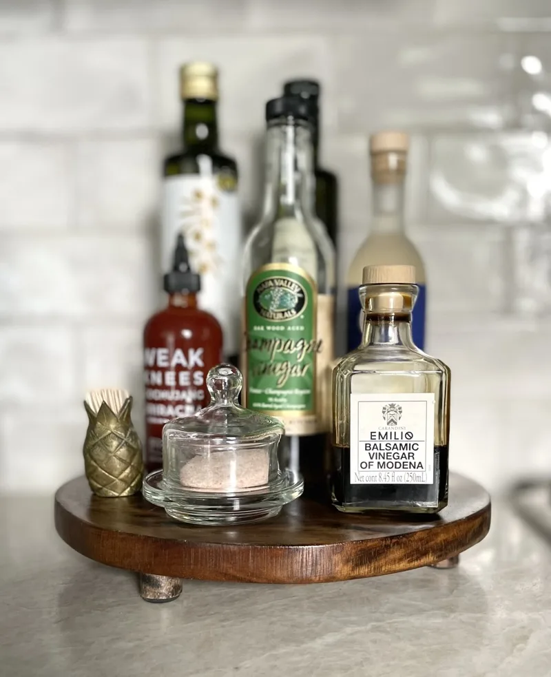 Wooden lazy Susan on the counter with olive oil, vinegars, and a brass pineapple accent