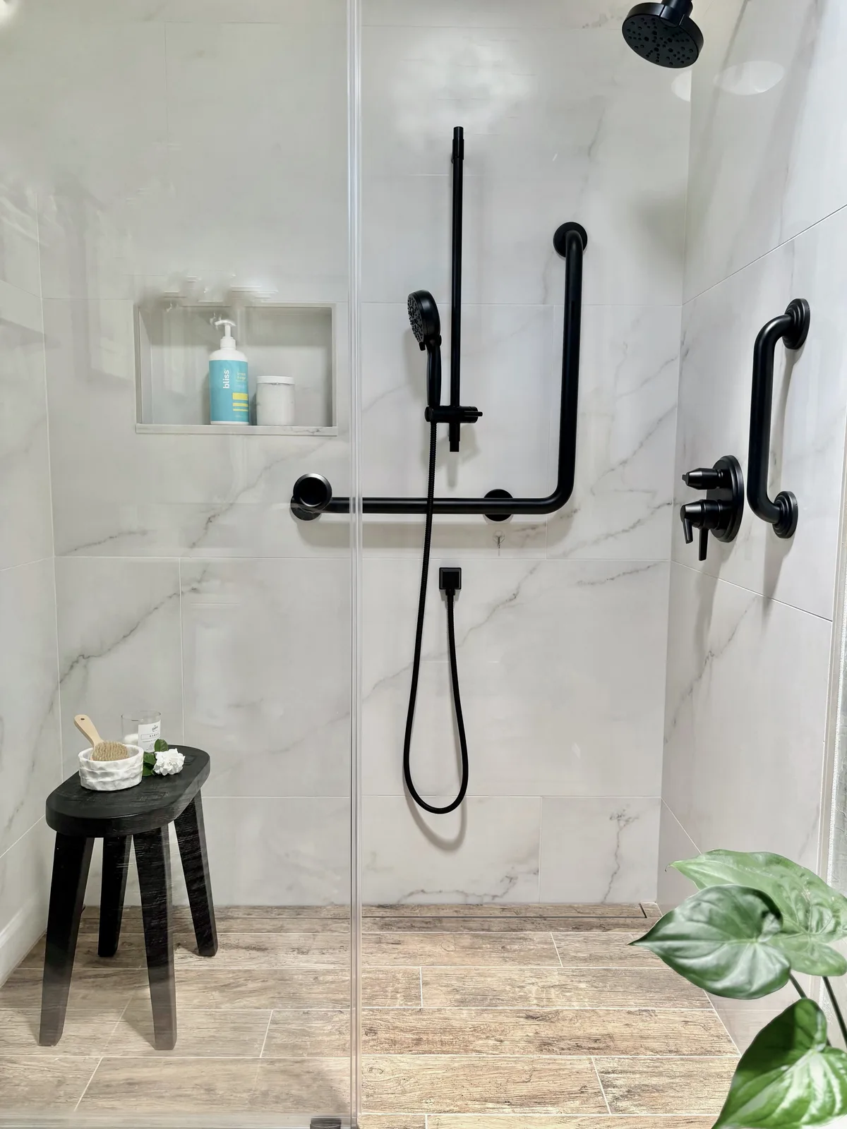 Curbless walk-in shower with marble tile, integrated matte black grab bars, handshower, and black shower stool