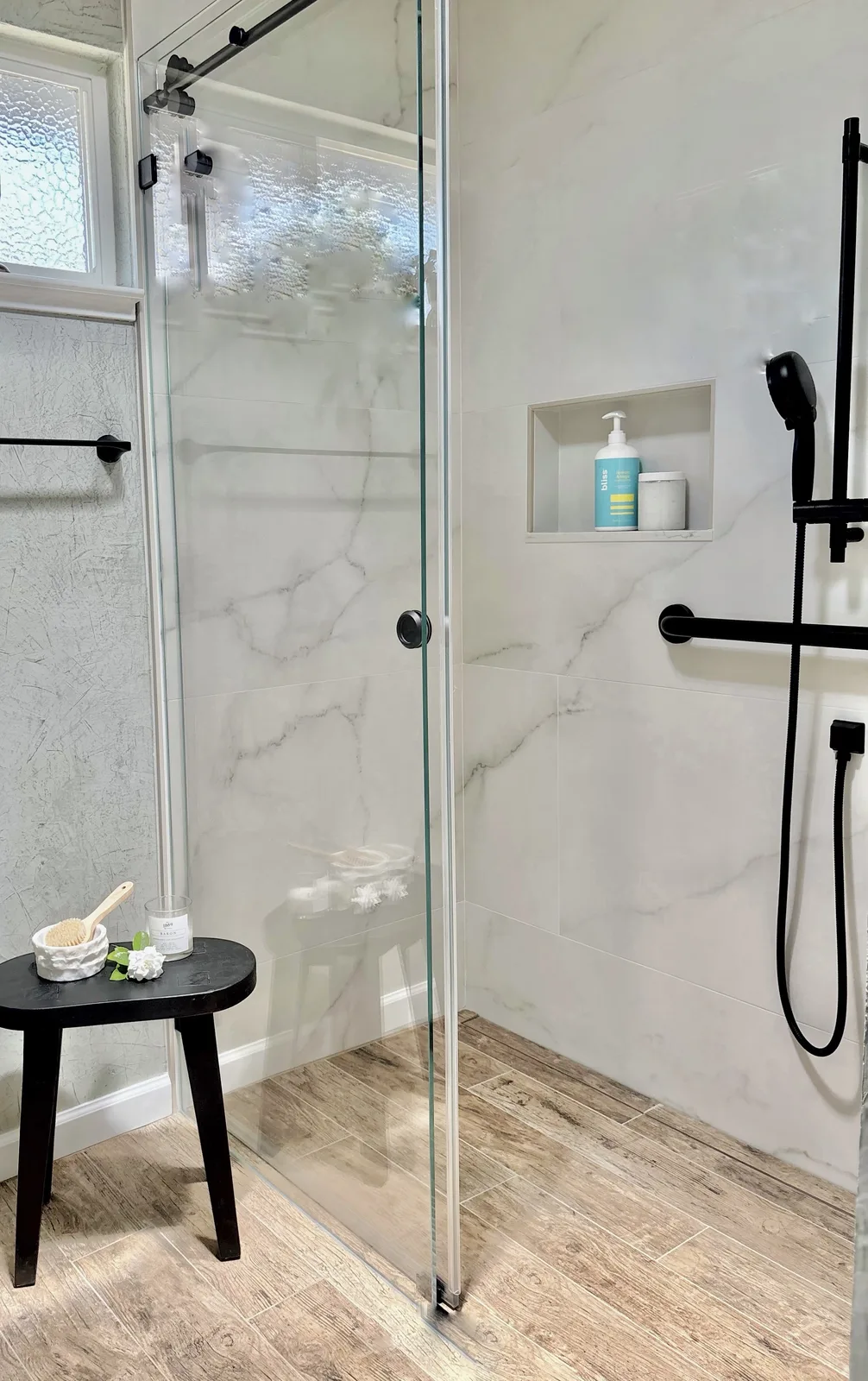 Frameless glass shower enclosure with marble tile, rain head, and black shower stool