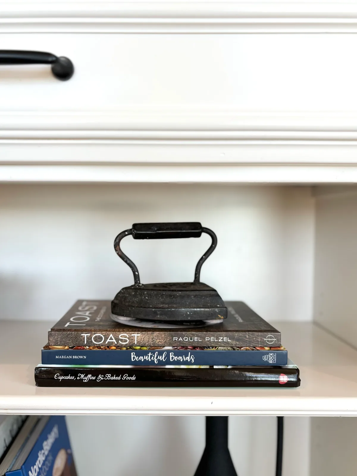 Iron doorstop with cookbooks including "Toast" on a white open shelf