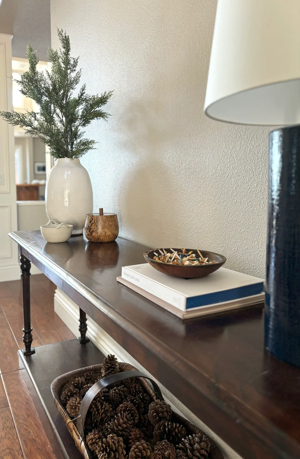 Dark console table with pinecone display, ceramic vase with evergreen, and navy lamp