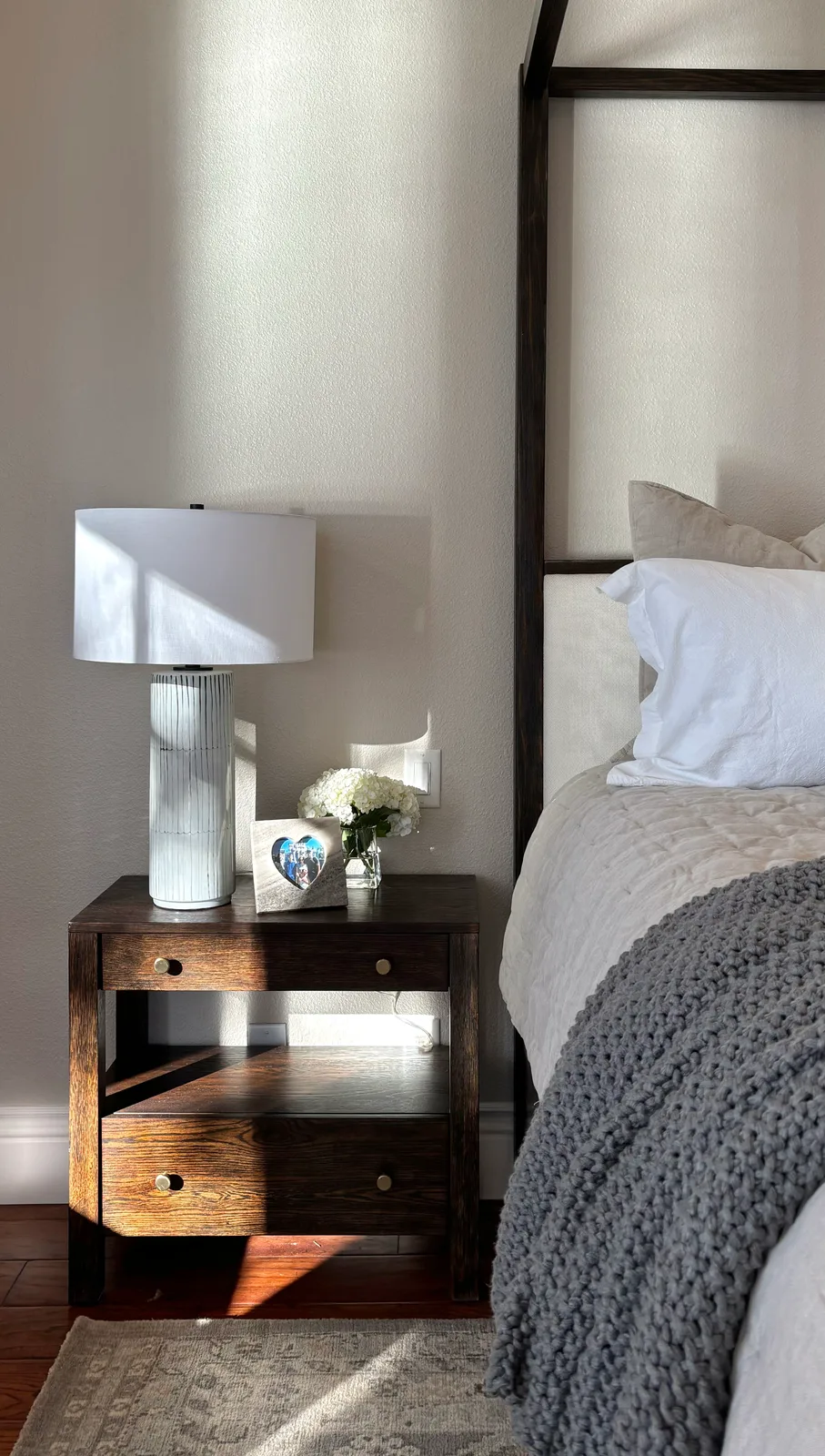 Reclaimed wood nightstand with white ceramic lamp, hyacinth, and grey chunky throw
