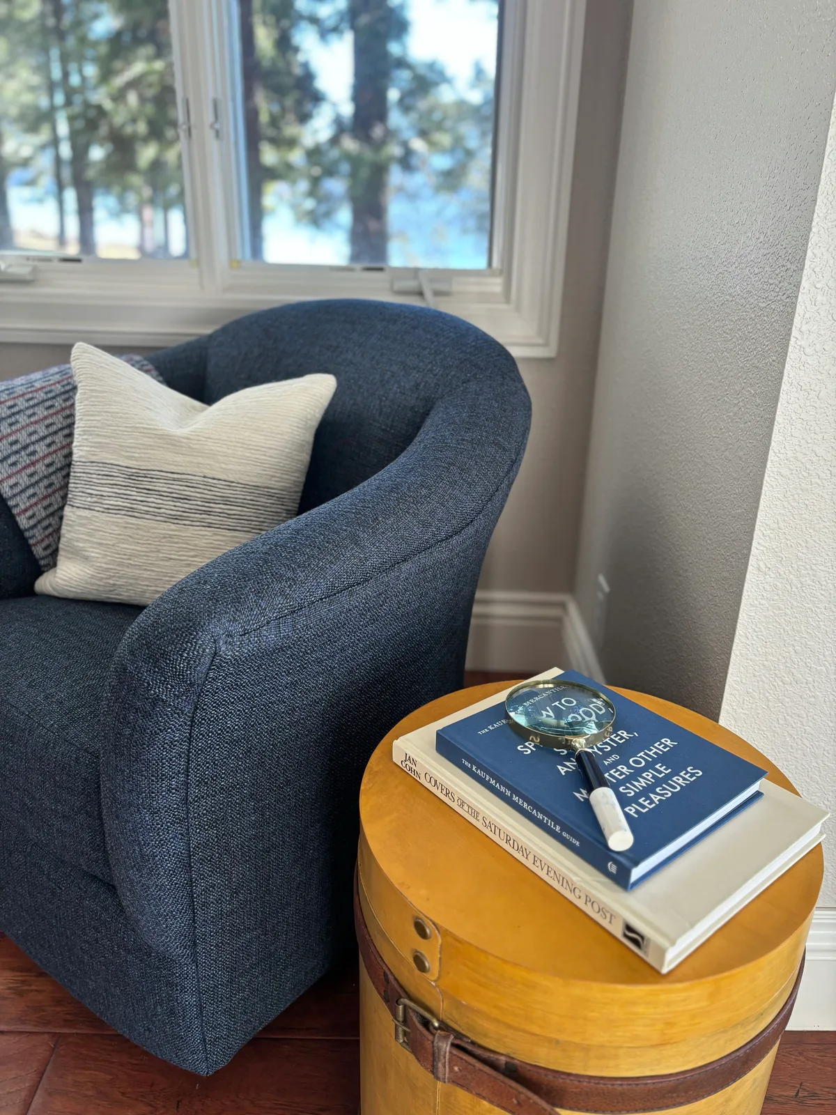 Blue linen reading chair with striped pillow beside a leather-wrapped drum side table