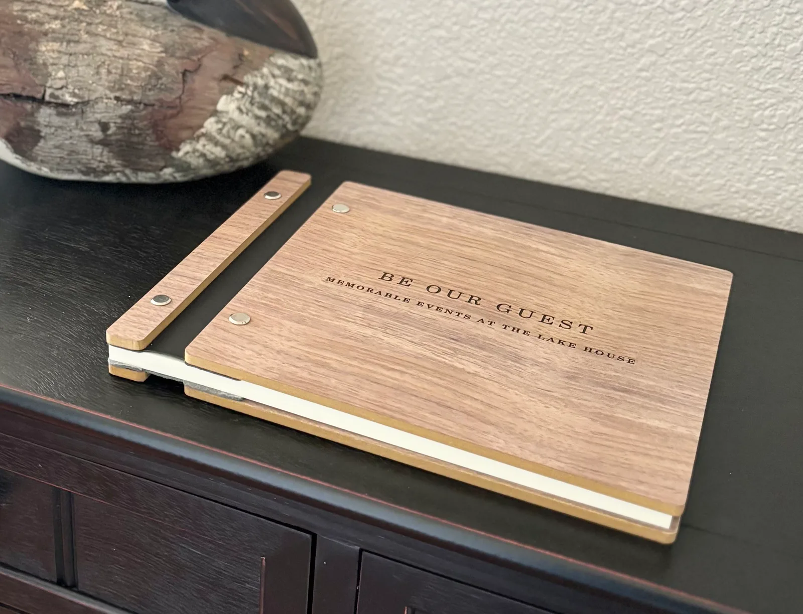 Walnut "Be Our Guest" lake house memory book with brass binding on a dark console