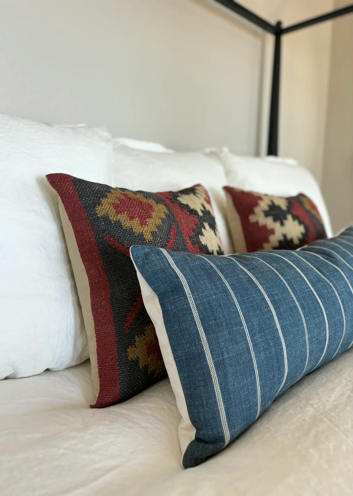Black iron canopy bed with layered Kilim accent pillows in cream, rust, and navy
