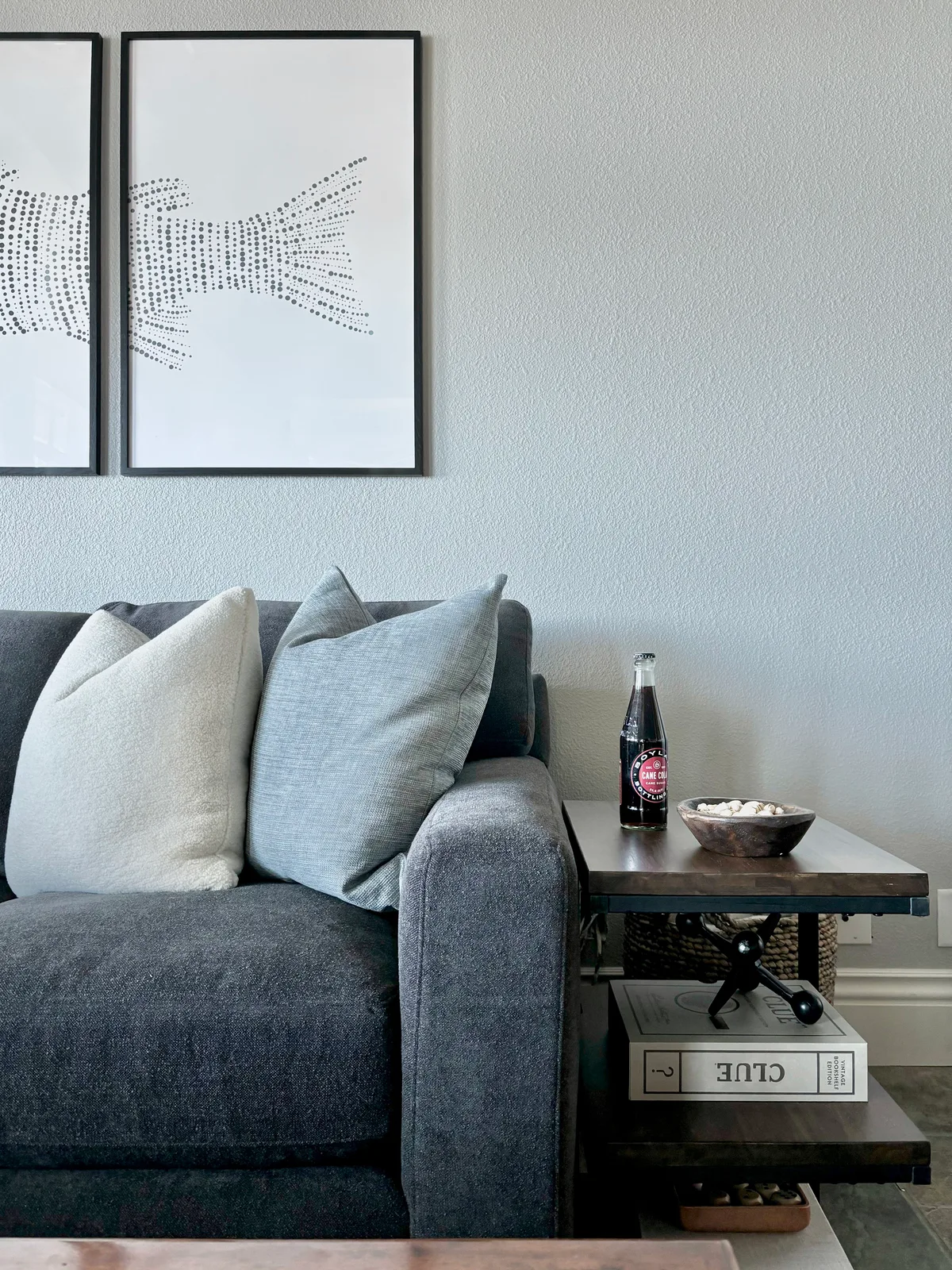 Fish-pattern artwork above a grey linen sofa with travel books on a dark shaker side table