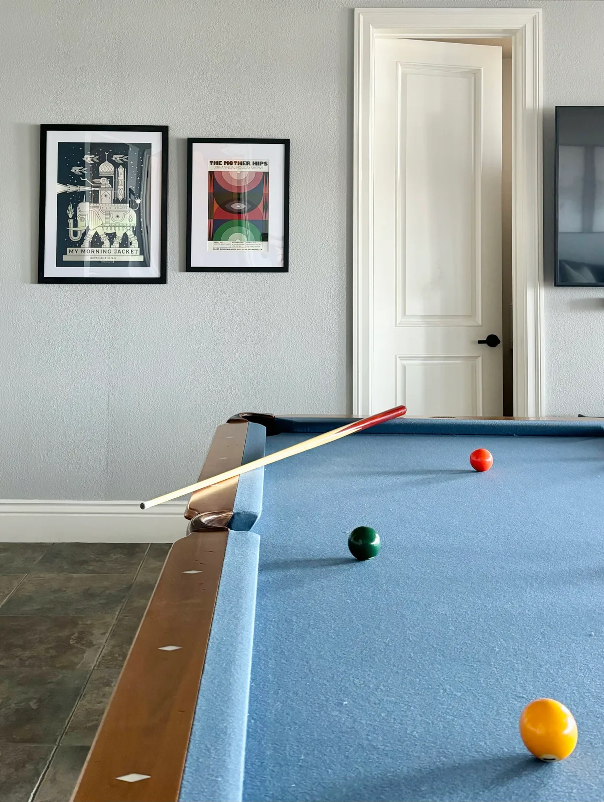 Pool table with cues on the rail and framed gallery art on the wall