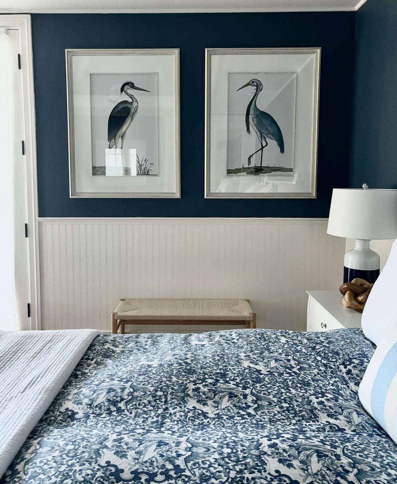 Navy accent wall with framed heron prints above a grey floral bed