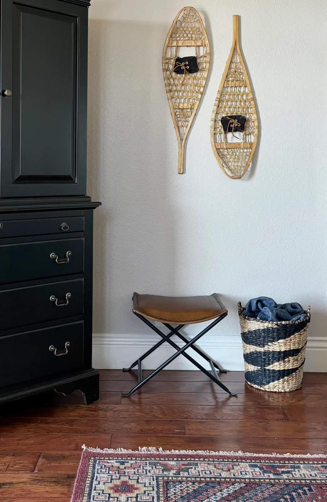 Black chest of drawers with vintage snowshoes mounted on the wall above a leather folding stool