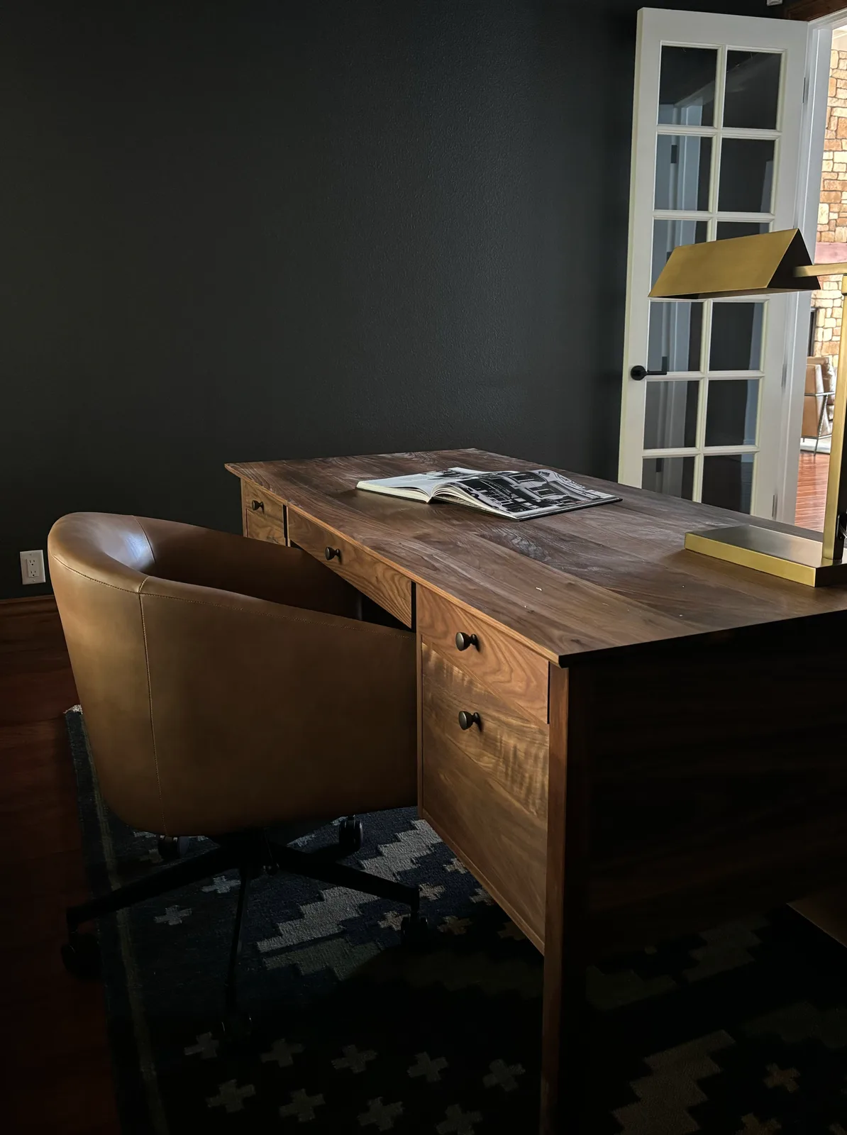 Handcrafted walnut desk with leather tumbler chair and brass desk lamp in a dark-walled study