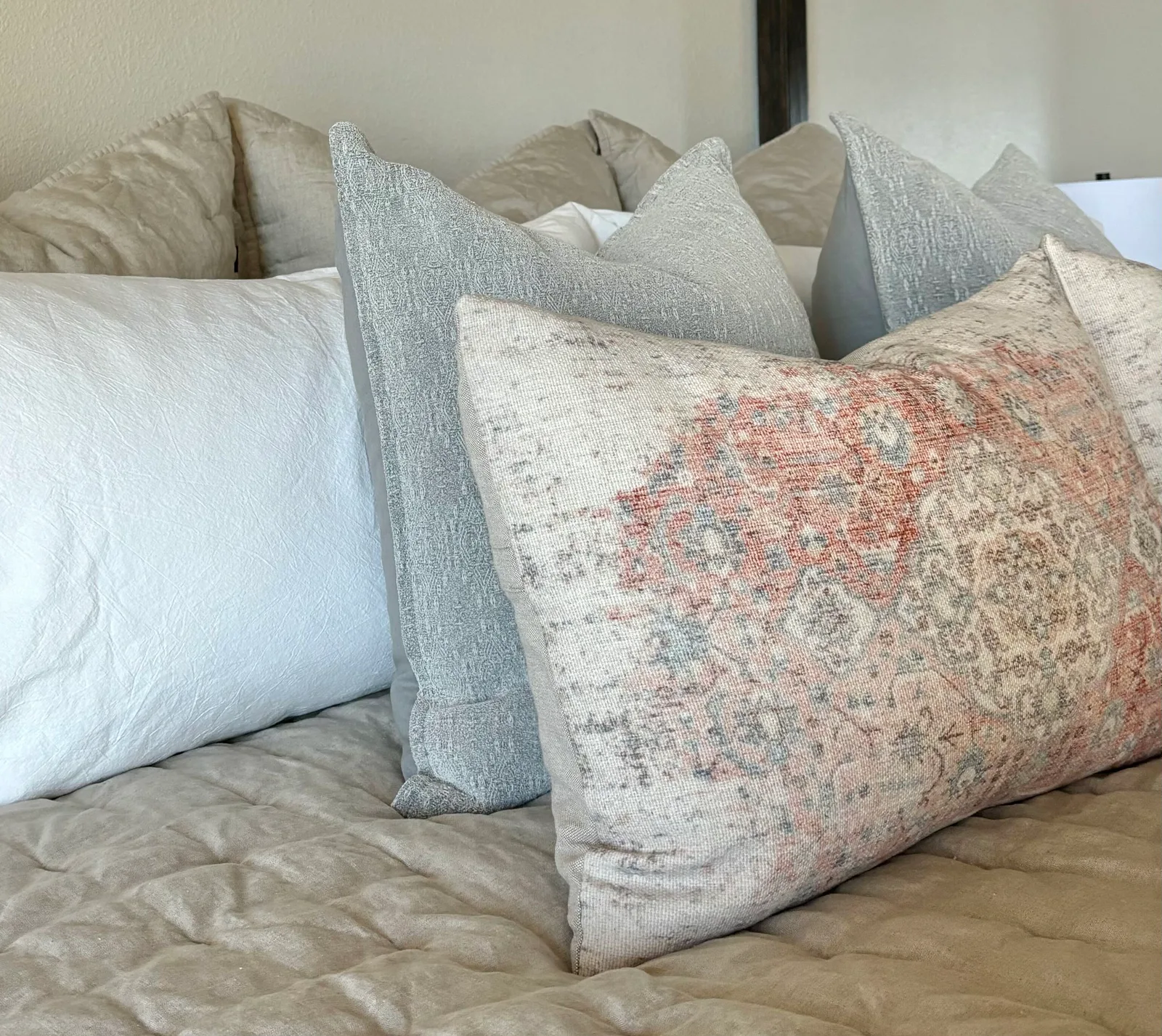 Bed pillow vignette with linen bolsters and a faded Persian-style lumbar on quilted bedding