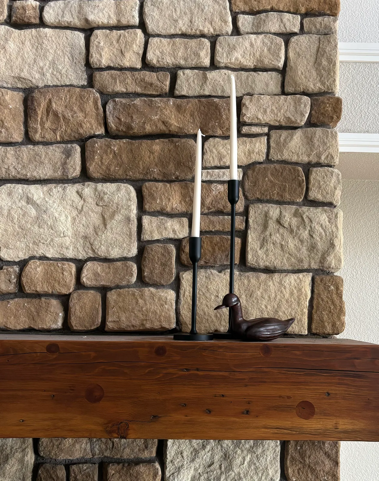 Stone fireplace wall with wooden mantel, bronze duck figurine, and tall iron candleholders