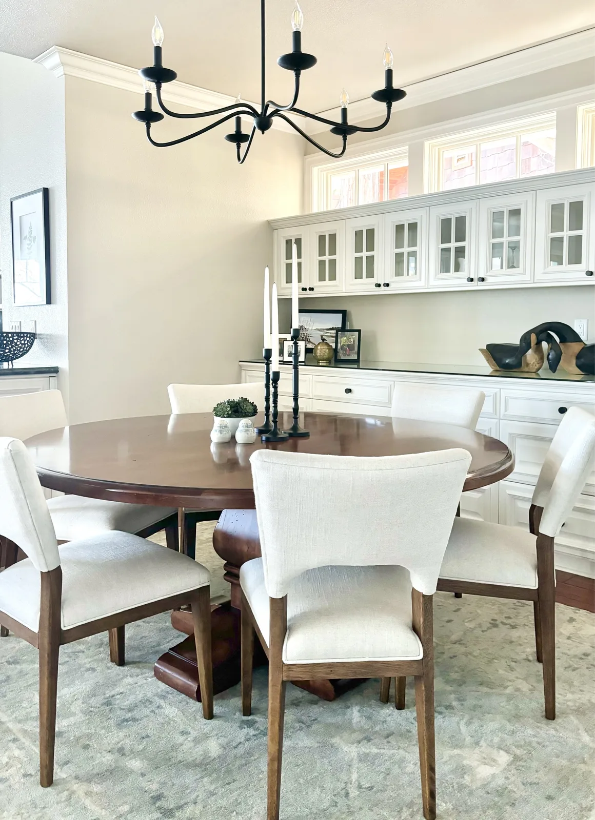 Formal dining room with black cottage chandelier, round wood table, and linen chairs