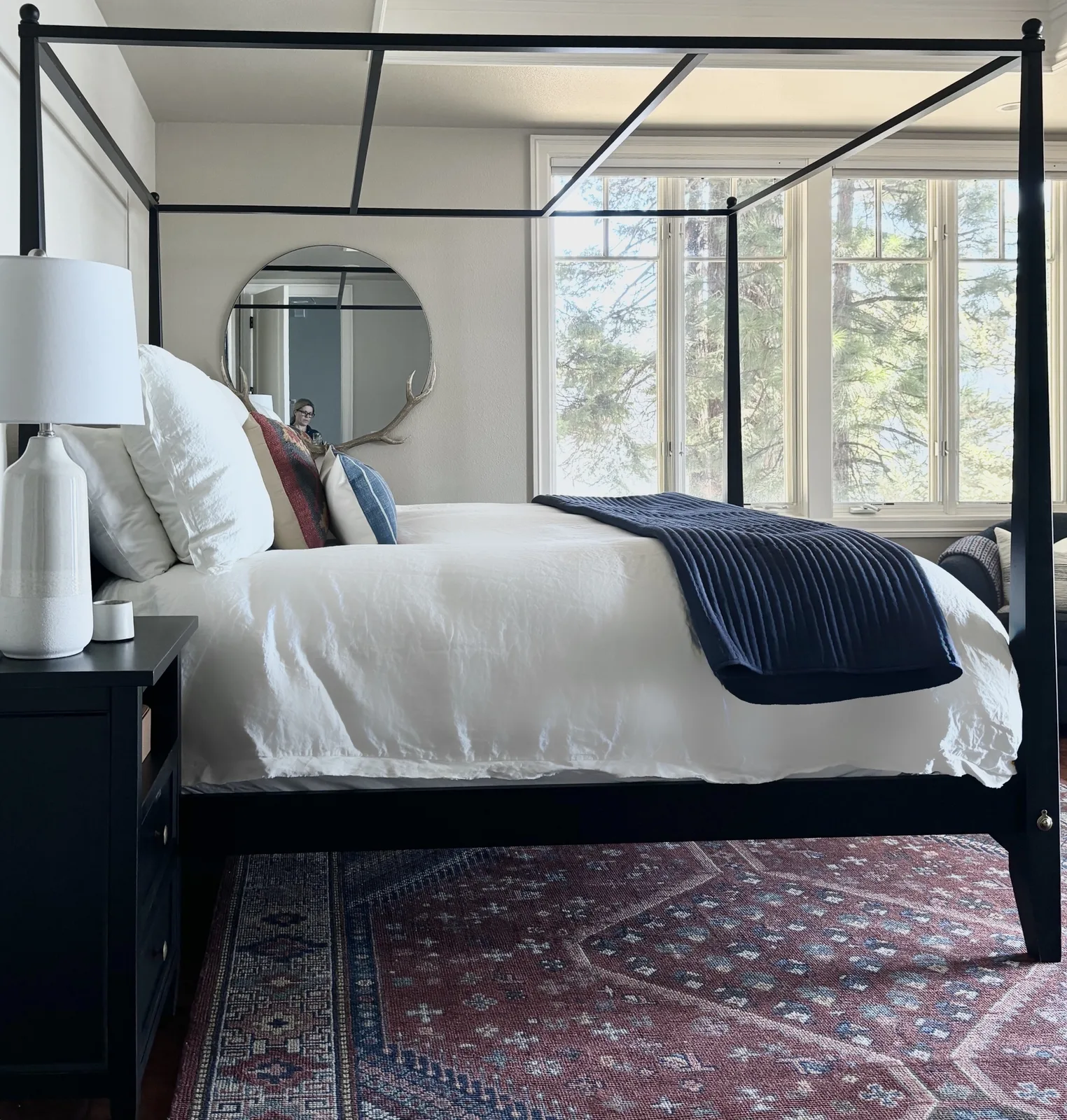 Black iron canopy bed with round mirror above nightstand and red Persian rug
