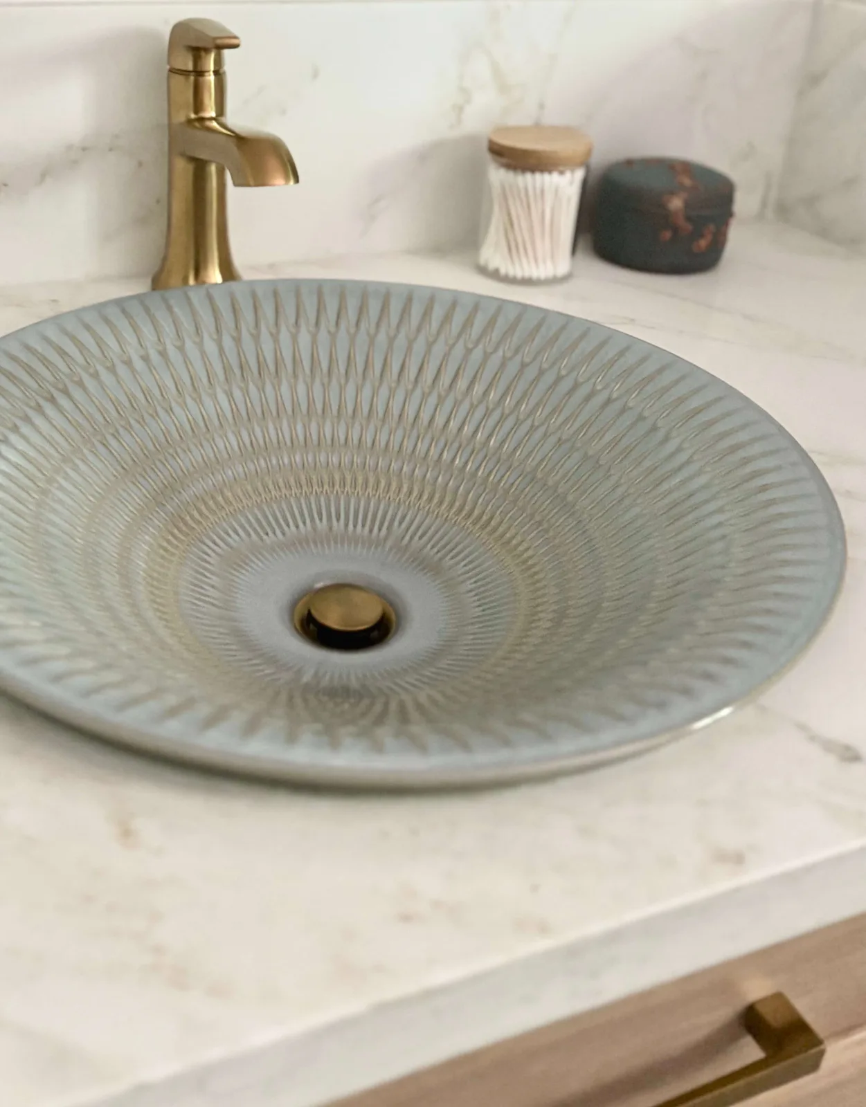Hand-glazed gray ceramic vessel sink with brass faucet on marble vanity