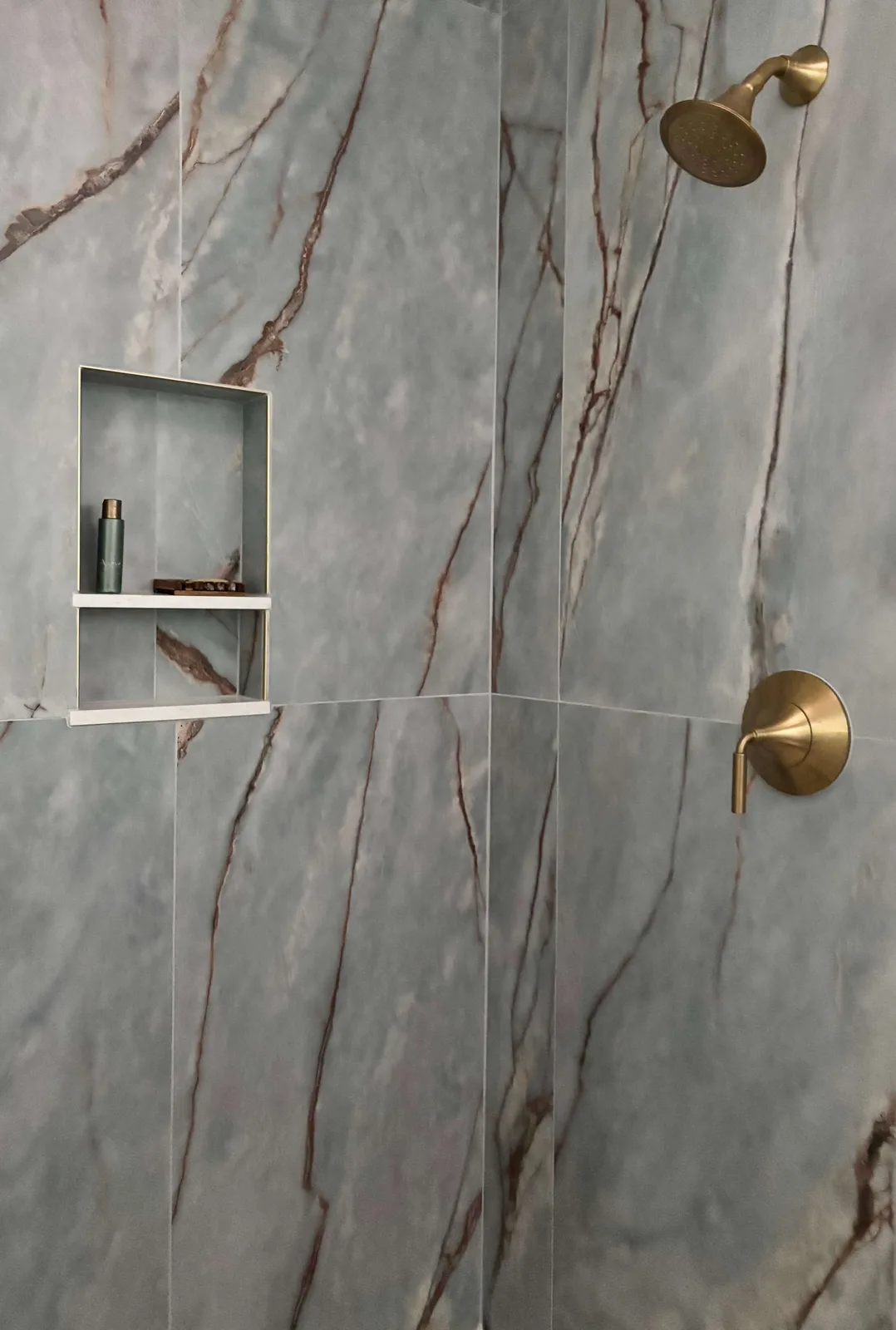 Deep River porcelain shower with veined blue marbling, brass shower head, and recessed niche