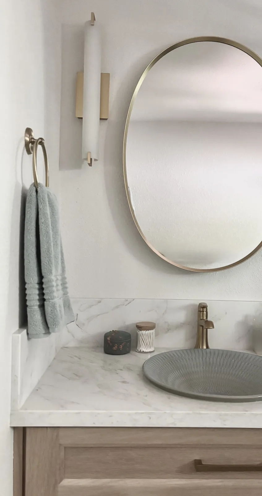 Round brass-framed mirror and brass wall sconces above the gray ceramic vessel sink