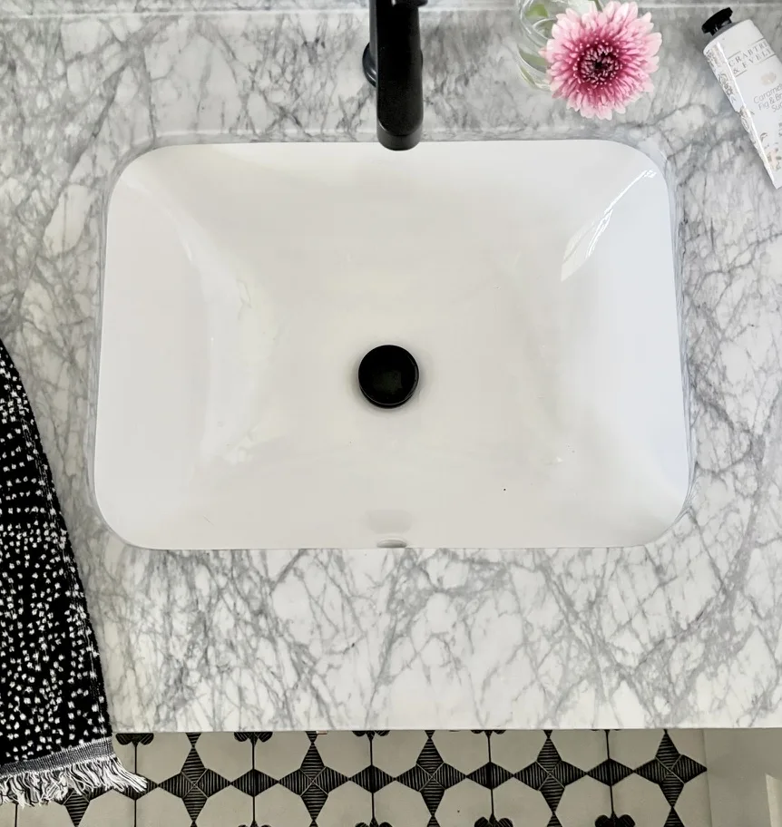 Top-down bathroom view: rectangular undermount sink on marble with black-and-white hex floor tile