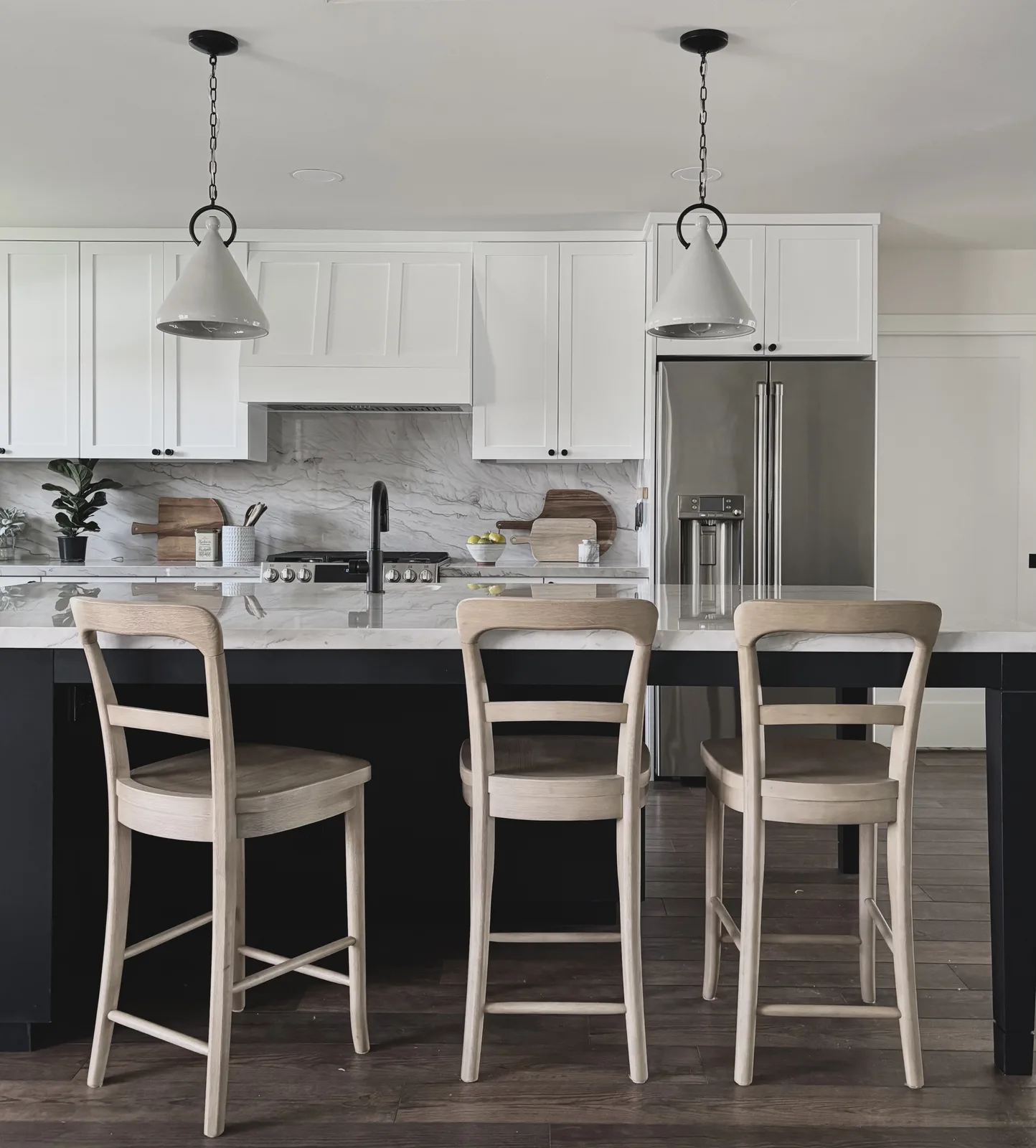 White kitchen island with three oak counter stools, pendant lights, and marble counters