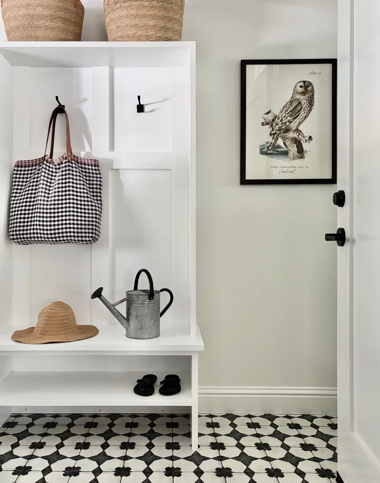 Mudroom built-in with checkered tile floor, woven baskets, and framed owl print