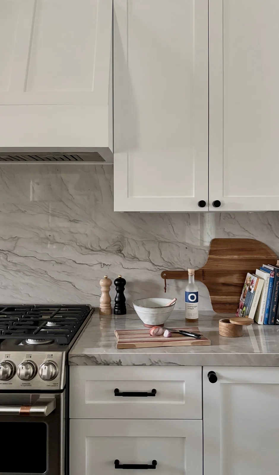 Gas range with stainless hood, marble backsplash, pepper mill, and wood cutting boards