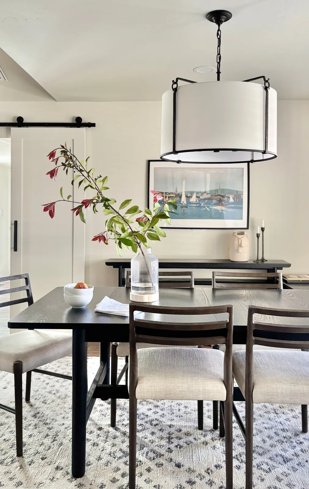 Modern dining room with drum pendant light, dark table, sailboat art, and barn door