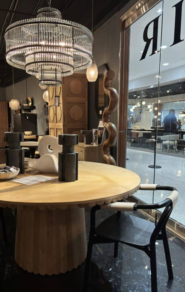 Modern dining area featuring a round wooden table with scalloped edges, black and white accents, and a large decorative chand