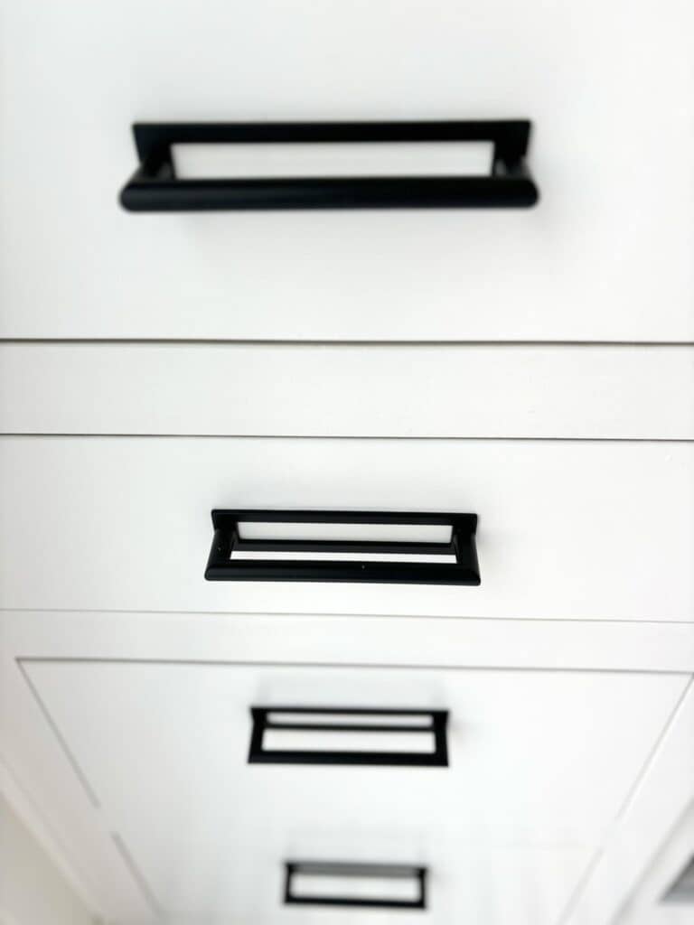 Modern kitchen cabinetry with sleek white finish and minimalist black handles. The design emphasizes clean lines and a contem