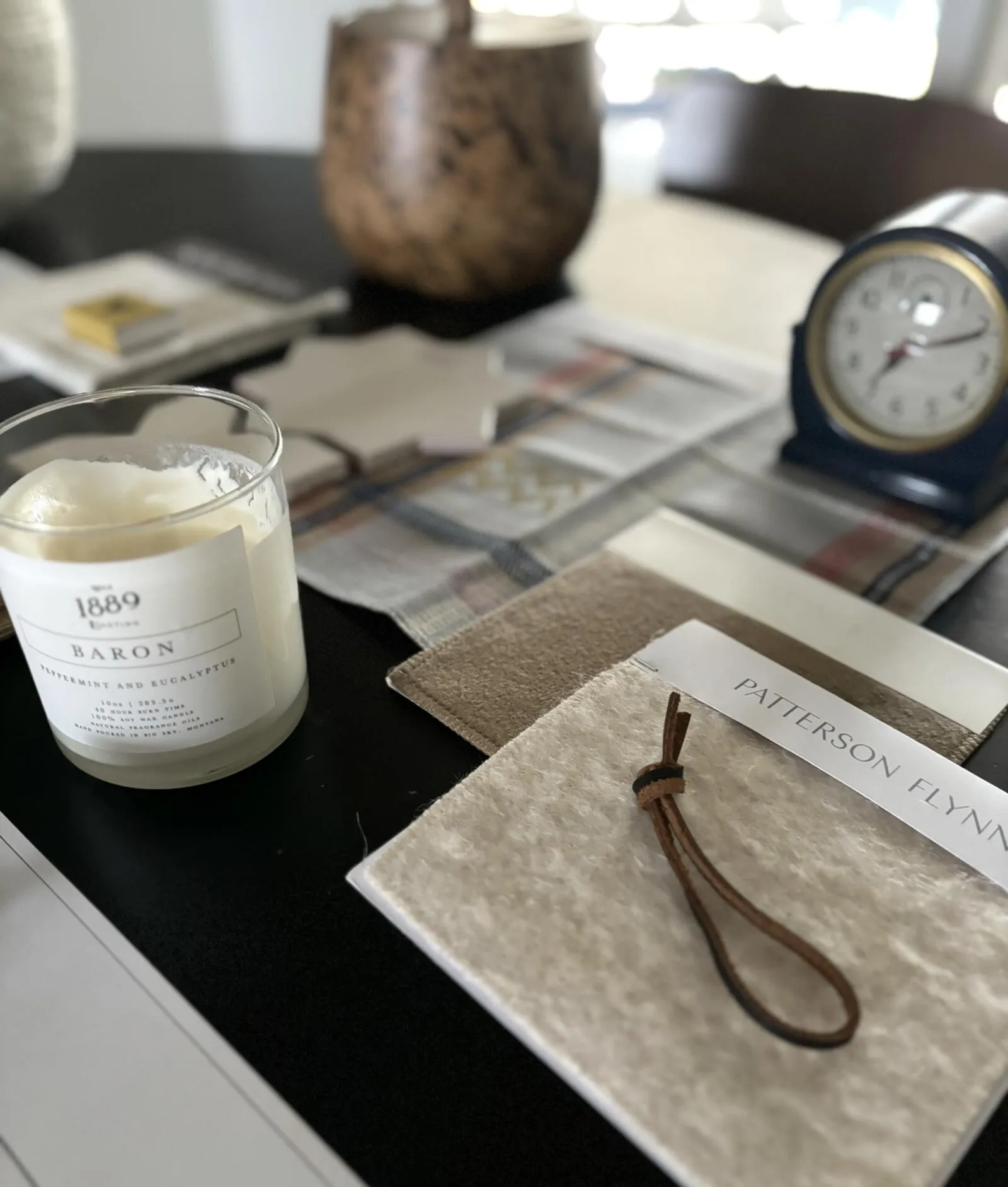 Close-up of a table with a candle, fabric swatches, a clock, and a decorative item, suggesting an interior design settin — San Mateo Atherton Sovereign Sanctuary Interior Design for the Atherton Estate
