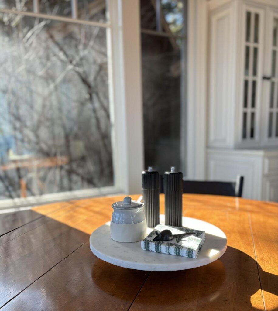 Bright, modern dining space featuring a wooden table with a marble serving tray, white ceramic container, and two black candl