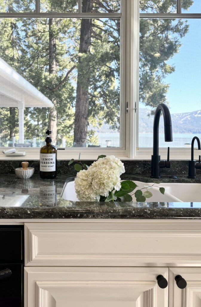 Modern kitchen with black fixtures and granite countertop, featuring large windows overlooking a natural landscape.