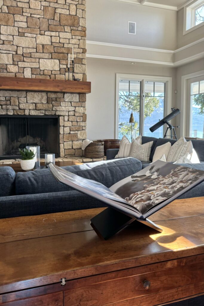 Cozy living room featuring a stone fireplace and large windows allowing natural light. Furnished with a dark sofa and a woode
