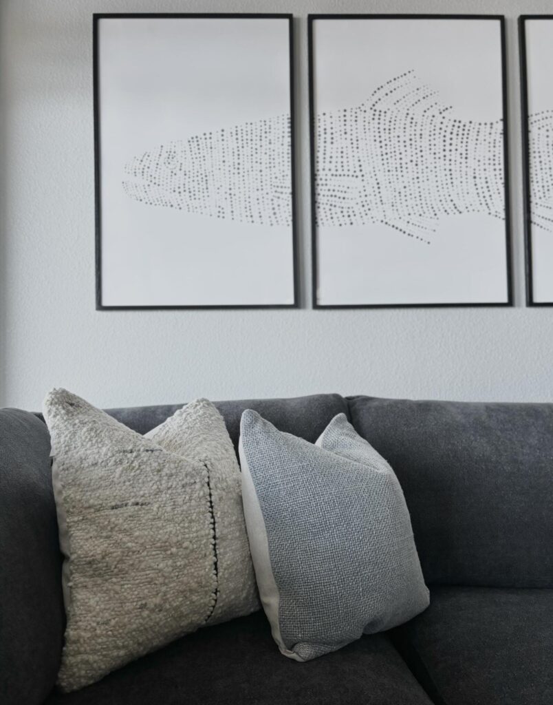 Modern living room featuring a dark gray sectional sofa with textured throw pillows and minimalistic wall art depicting abstr
