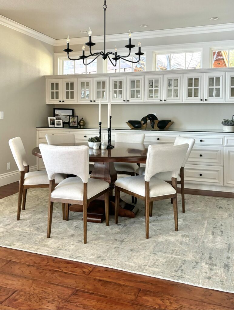 Modern dining area featuring a round wooden table surrounded by upholstered chairs. Light-colored cabinetry and a neutral rug