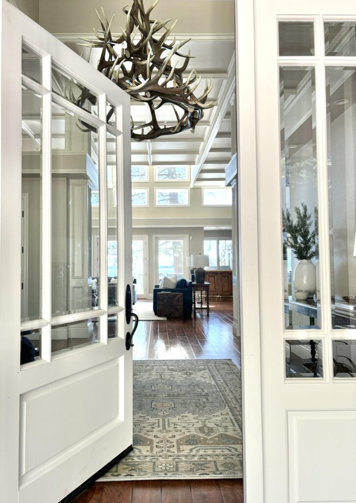 Modern entryway featuring large glass doors with white trim, leading to a spacious living area adorned with wooden flooring a