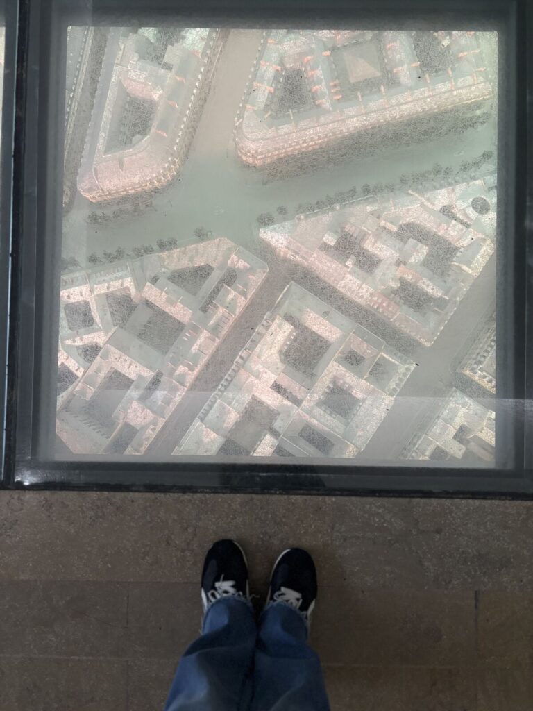 A transparent floor panel revealing a detailed, elevated view of an urban landscape with a grid layout of streets and buildin