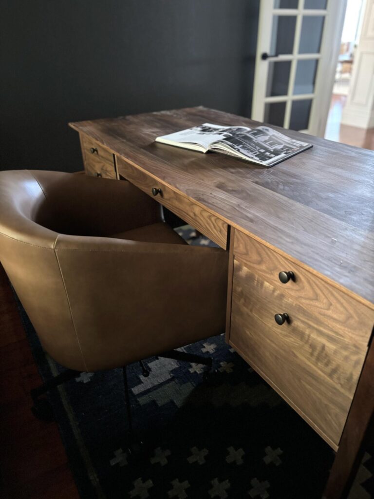 Contemporary workspace featuring a wooden desk with multiple drawers and a curved leather chair, set against a dark wall with