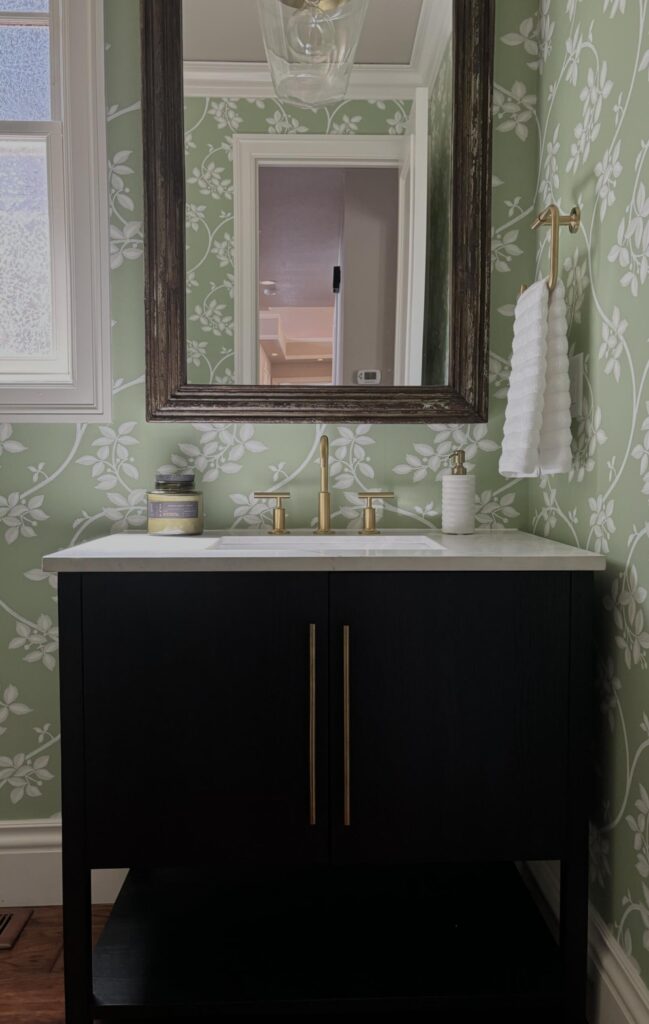 Modern bathroom with a dark wood vanity and gold fixtures, featuring floral-patterned green wallpaper that adds a fresh, cont