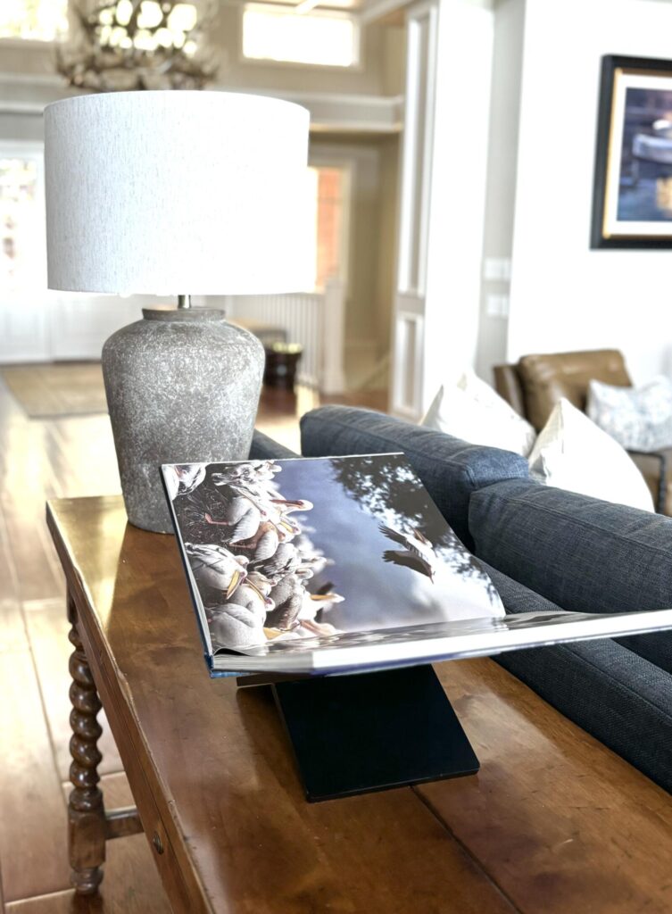 Cozy interior featuring a wooden table with a textured gray lamp, an open photo book, and a sectional sofa. The space has war