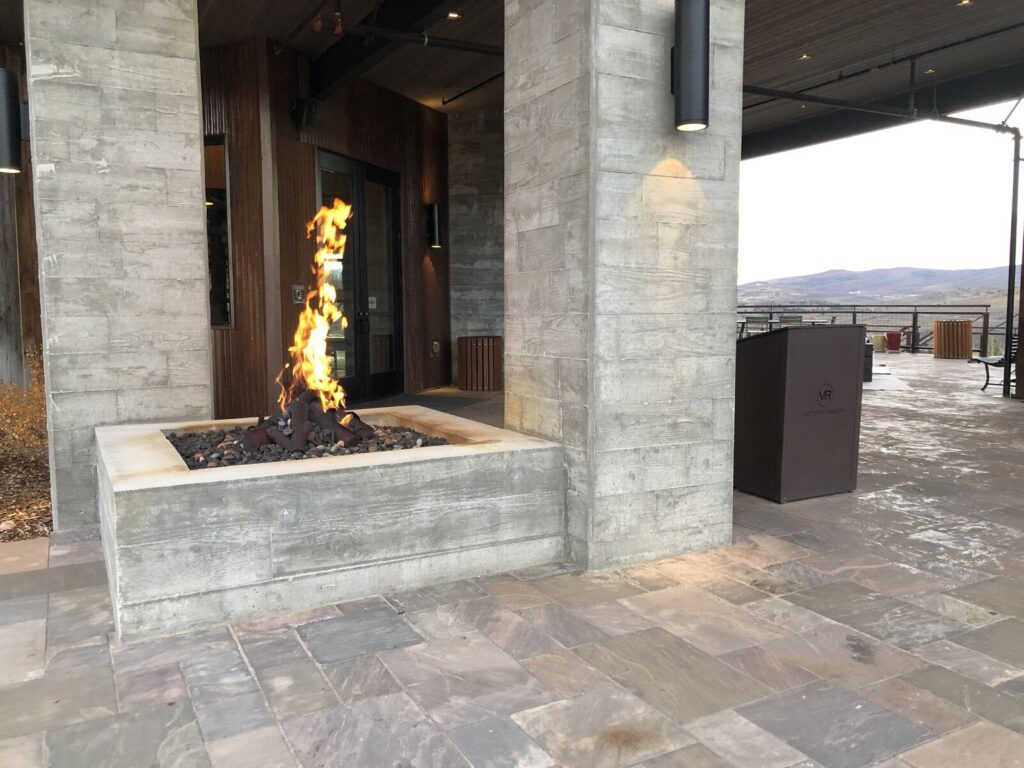 Modern outdoor lounge area featuring a fire pit surrounded by natural stone landscaping. The structure has a contemporary aes