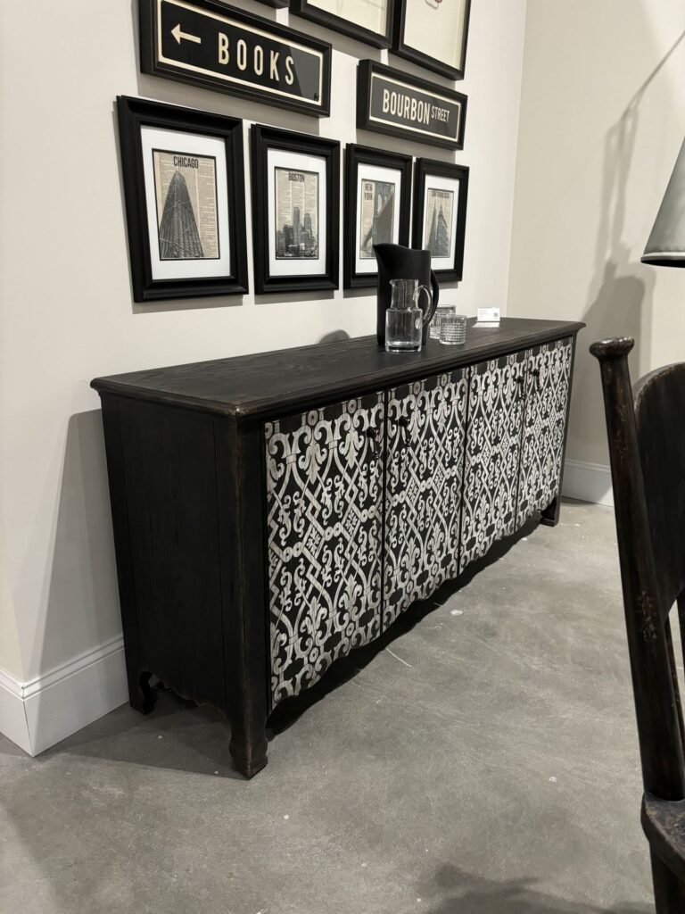 Modern interior featuring a dark wooden sideboard with intricate white patterns and a gallery wall of framed prints, creating
