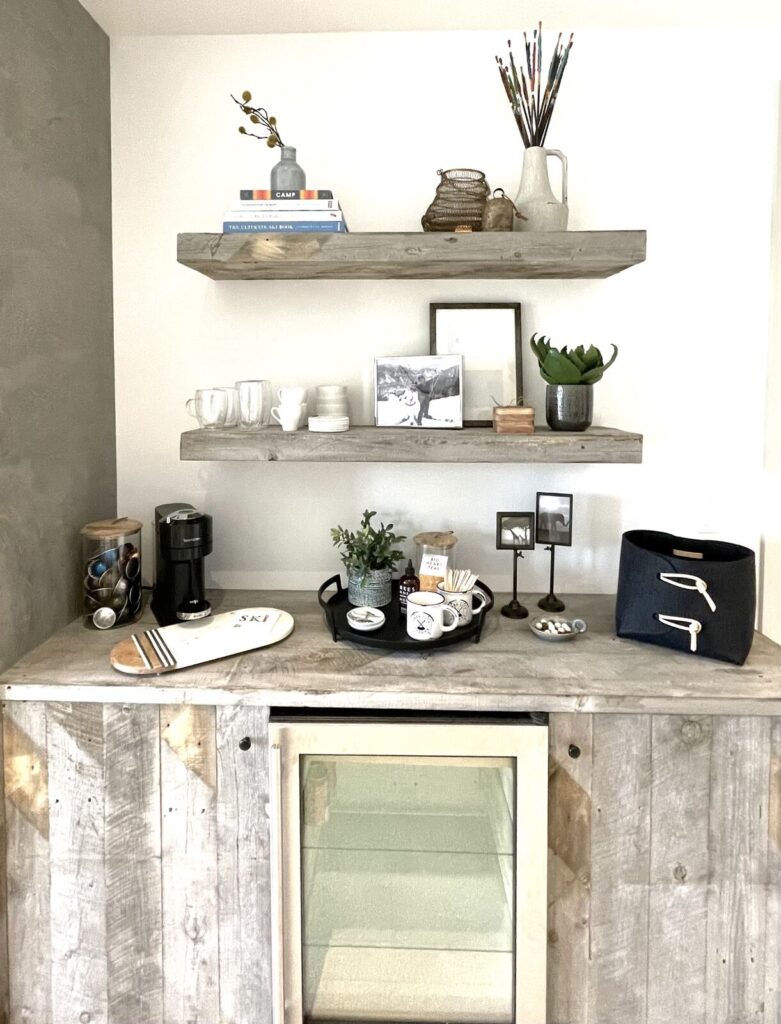 Modern home bar with minimalist design featuring wooden shelves, a concrete counter, and neutral decor. The space is bright a
