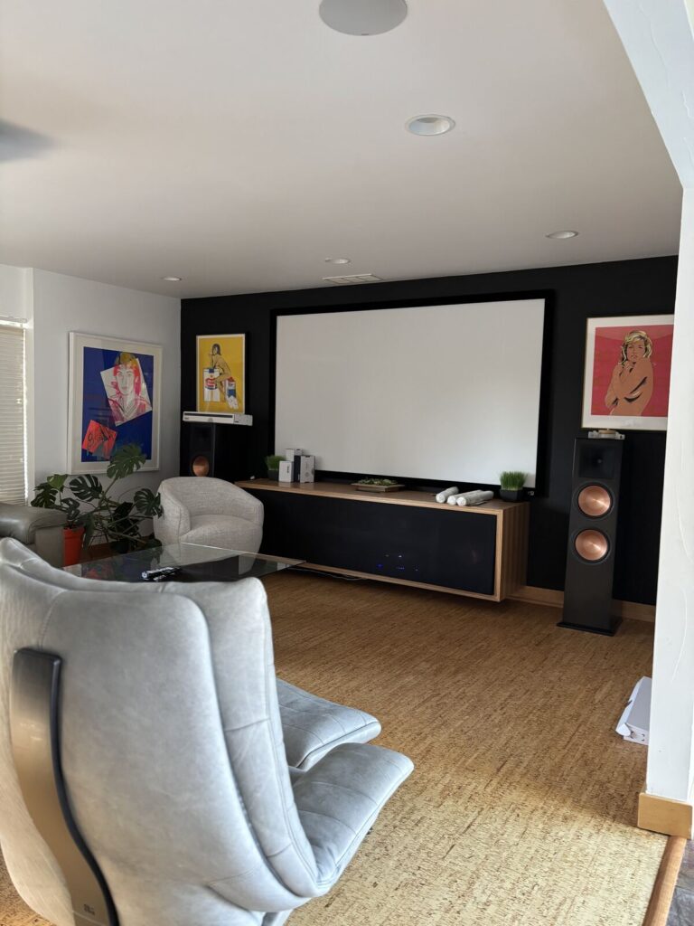 Modern home theater with a large projection screen, minimalist wooden console, and stylish audio speakers. The room features