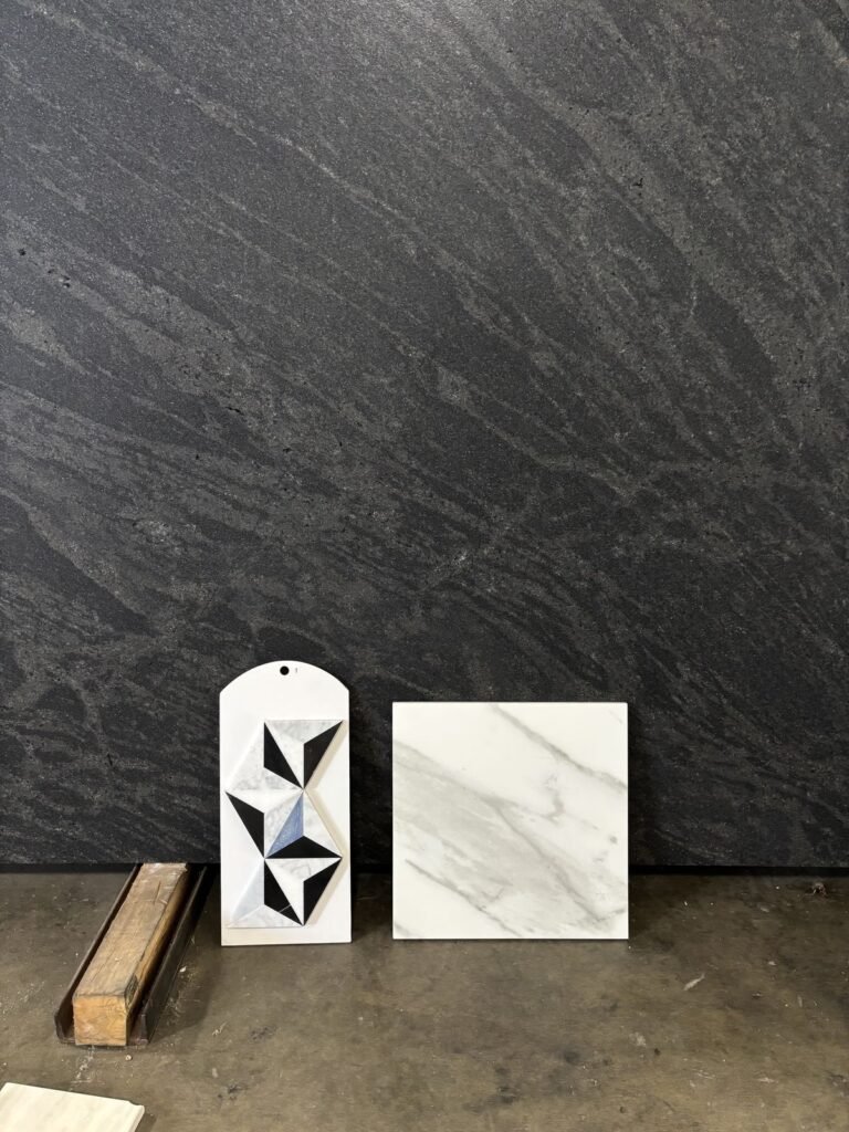 Contemporary interior design showcase featuring a textured black wall with dark veining. Two marble samples, one with a geome