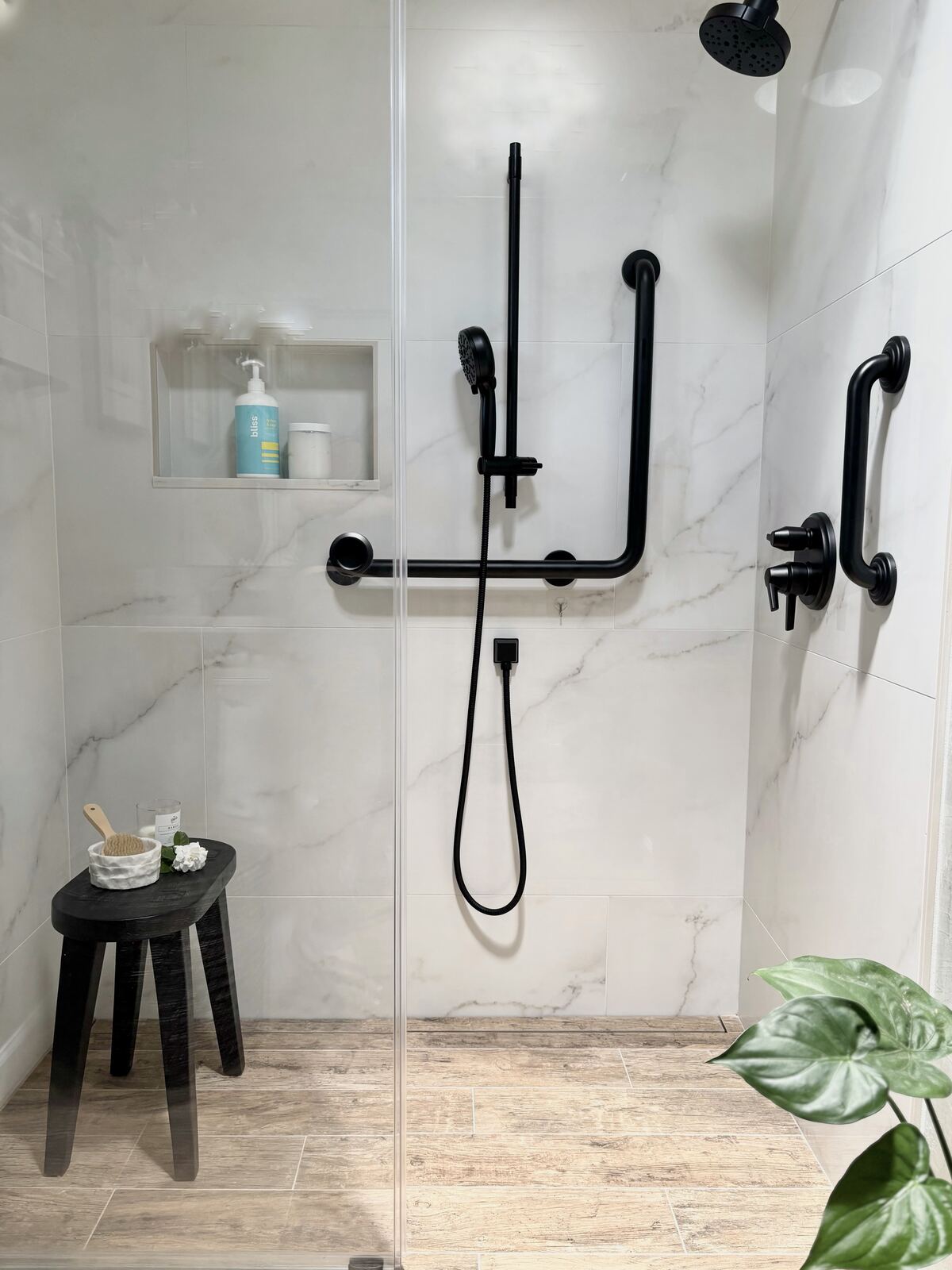 A modern bathroom shower with marble walls, black fixtures, and integrated grab bars
