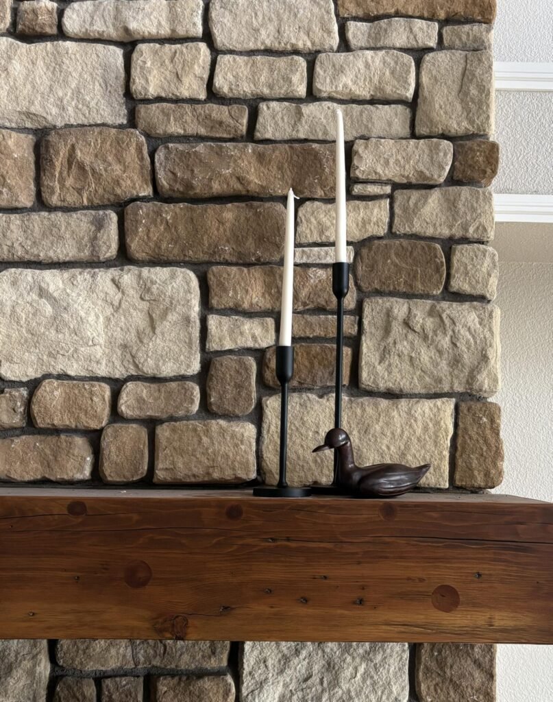 Natural stone fireplace with a rustic wooden mantel, featuring tall candlesticks and a decorative duck figurine.