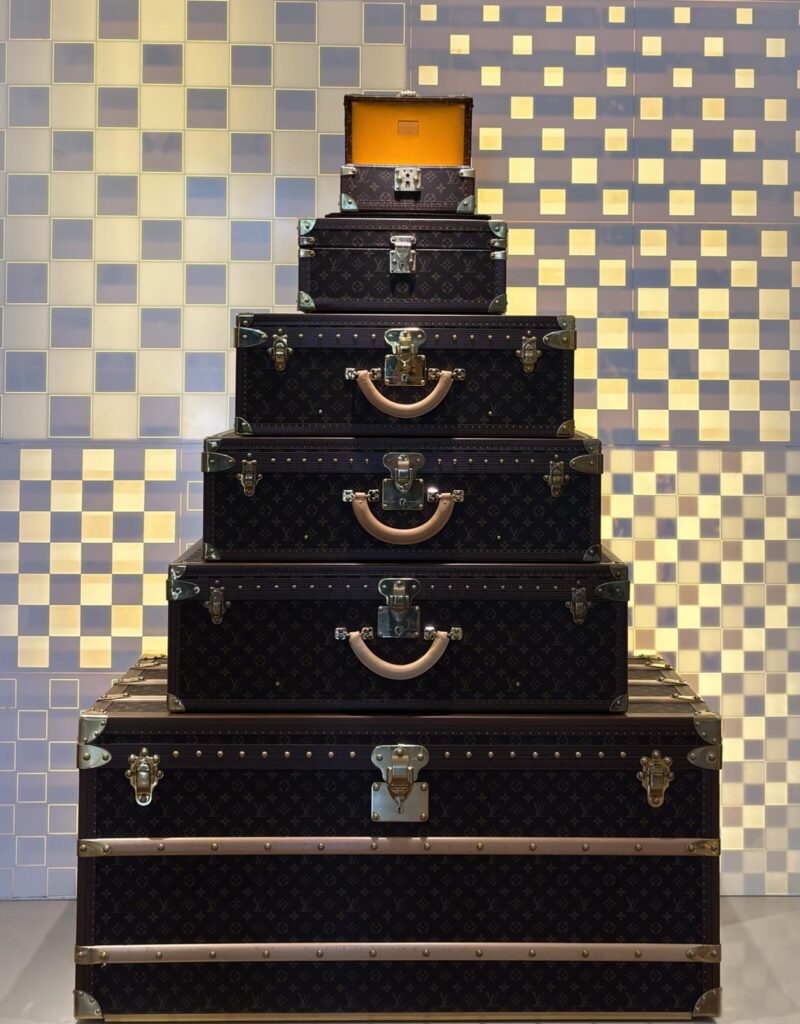 A modern display featuring a stacked arrangement of vintage-style leather suitcases with metal trims against a textured backd