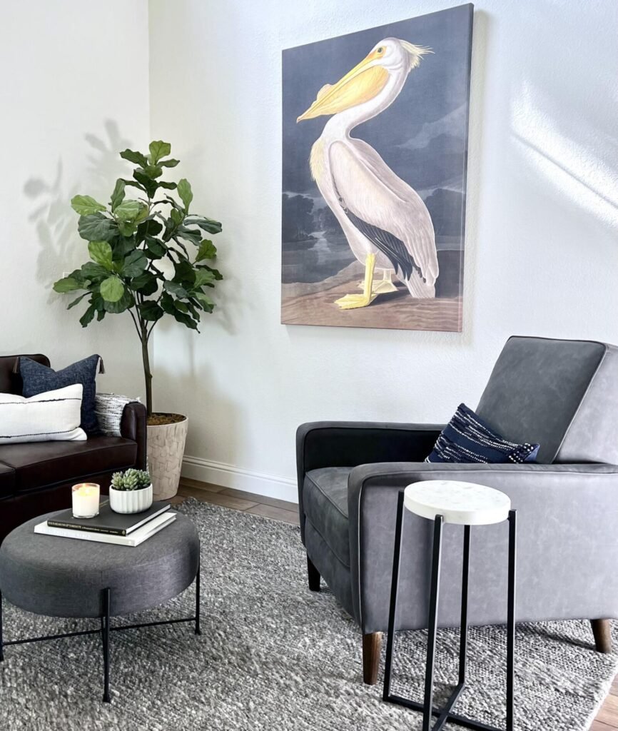 Modern living room featuring a gray accent chair and a brown leather sofa, with a large painting of a pelican on the wall. Th